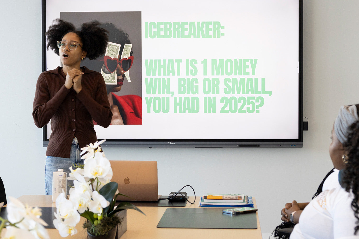 A woman presenting in front of a screen with an icebreaker question, in a classroom setting.